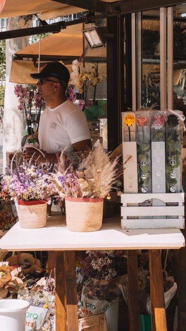 A floral display at Edgware Florist featuring a variety of fresh flowers arranged in woven baskets on a white table. The arrangement includes soft lavender and purple flowers, complemented by white an